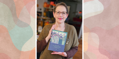 Kvinna med glasögon håller en bok och ler mot kameran, suddig bakgrund inomhus.