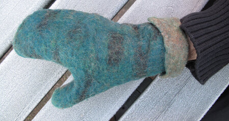 En hand med en blågrön stickad vante vilar på en frostig träbänk utomhus.