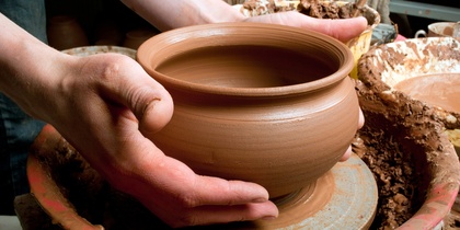 Två händer formar en lerkruka på en drejskiva i en keramikverkstad.