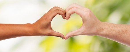 Två händer av olika hudfärg formar ett hjärta mot en suddig grön bakgrund.