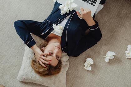Person i pyjamas ligger på golvet med laptop och pappersnäsdukar omkring sig.