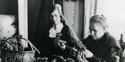 Två kvinnor sitter vid ett bord och arbetar med garn, traditionell miljö, svartvit bild.