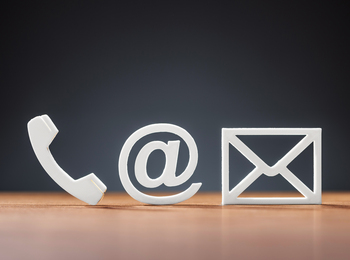 Tre vita symboler för telefon, e-post och brev på ett träbord mot mörk bakgrund.