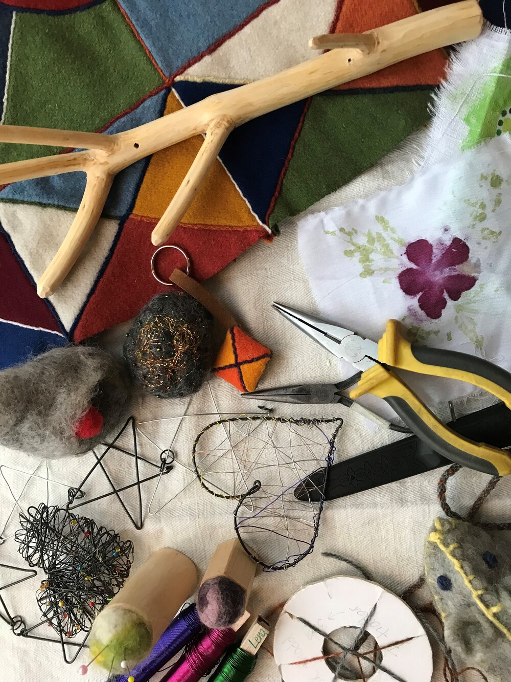 Material och verktyg för hantverk, inklusive tråd, tång, filt, trä och färgglad tygbit på ett bord.