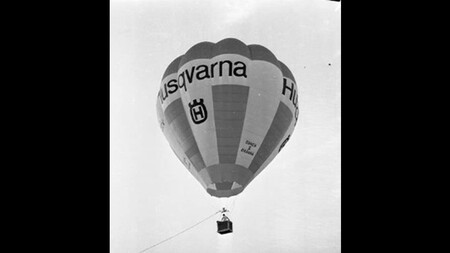 En varmluftsballong med texten 'Husqvarna' svävar i luften mot en ljus himmel.