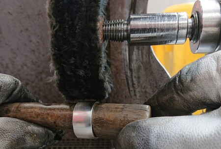 En person polerar en metallring med en roterande polermaskin och håller ringen med handskar.