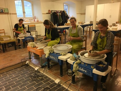 Fyra personer sitter vid drejskivor och arbetar med lera i en ljus keramikverkstad.