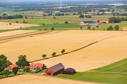 Landskapsvy över åkrar och bondgårdar med röda hus och lador på den svenska landsbygden.