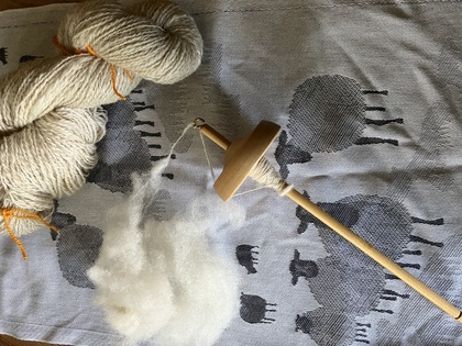 En slända, ull och spunnet garn ligger på en handduk med fårmotiv.