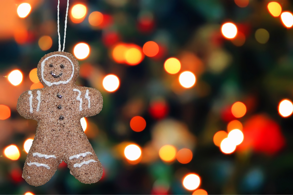 En pepparkaksgubbe hänger i ett snöre framför en suddig bakgrund med färgglada julbelysningar.