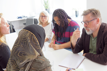 Fem personer sitter runt ett bord och diskuterar i ett ljust kontorsrum.