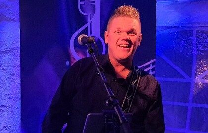 En person spelar gitarr och sjunger i mikrofon på en scen med blå belysning.