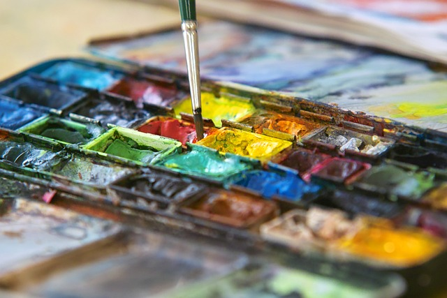 Närbild av en färgpalett med vattenfärger och en pensel som doppas i röd färg.