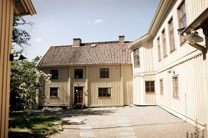 Innergård med ljus träbyggnad, röda takpannor och grusgång i soligt väder.