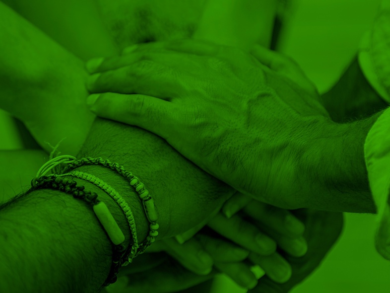 Flera händer lagda ovanpå varandra i en gest av samarbete, bilden har ett grönt färgfilter.