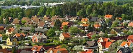 Färgglada villor med röda och gula tak i ett lummigt bostadsområde, omgivna av skog och berg i bakgrunden.