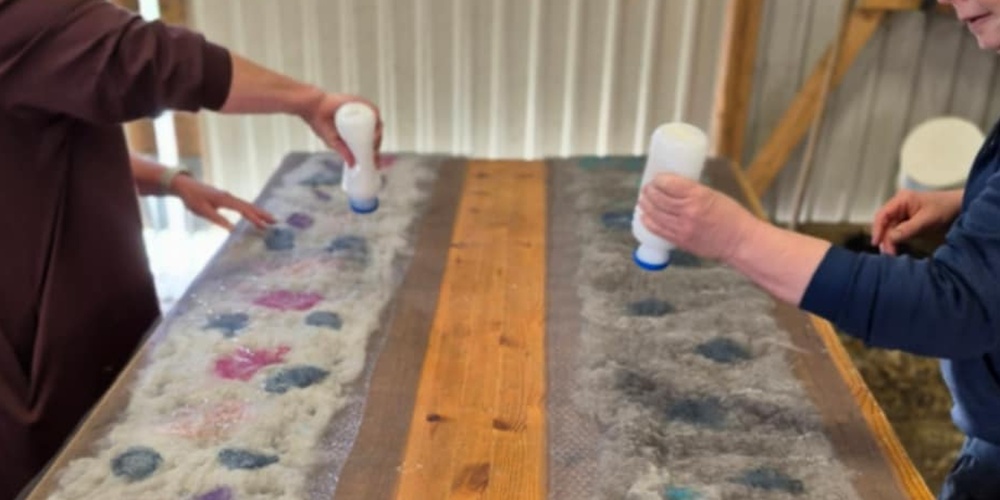Två personer arbetar med ull på ett bord, troligen under en tovningsworkshop.