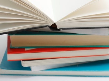 En hög med böcker där den översta boken är uppslagen och resten är stängda, mot vit bakgrund.