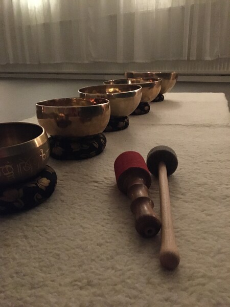 Fem tibetanska klangskålar står på rad på en matta med två klubbor framför dem i ett dämpat rum.