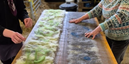 Två personer arbetar med ull på ett bord, troligen under en tovningsworkshop.