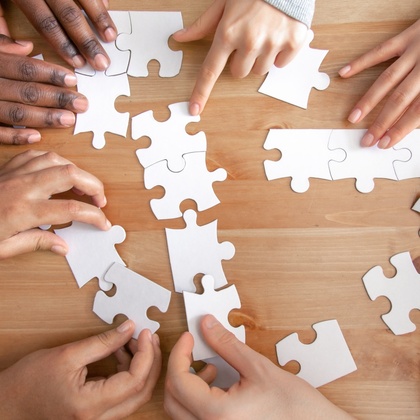 Flera händer samarbetar för att lägga ett pussel på ett trägolv.