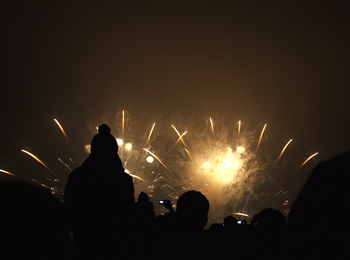 Silhuetter av människor tittar på ett fyrverkeri mot en mörk natthimmel.