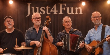 Fyra musiker spelar på scen med trummor, kontrabas, dragspel och gitarr inför en applåderande publik.
