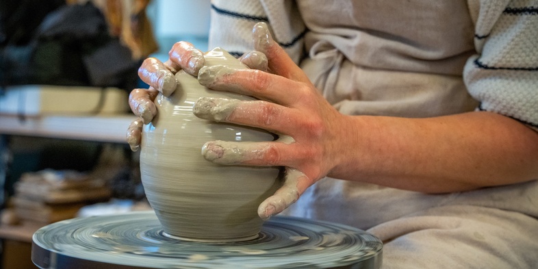 En person formar lera på en drejskiva i en keramikverkstad.