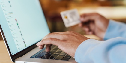En person använder en bärbar dator och håller ett kreditkort, troligen för onlineköp.