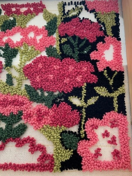 Närbild av ett broderi med blommönster i rosa, rött, grönt och svart på vit botten.