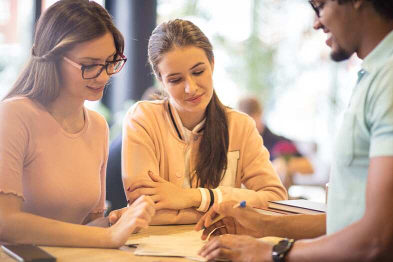 Tre personer diskuterar och tittar på ett papper på ett bord medan en av dem skriver på papperet.