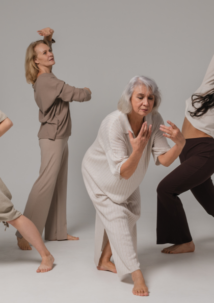 Fyra kvinnor i olika åldrar dansar barfota i mjuka, neutrala kläder mot en ljus bakgrund.