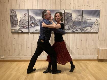 Ett par dansar tillsammans i ett ljust rum med trägolv och konst på väggen bakom dem.