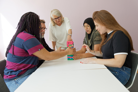 Fyra personer sitter runt ett bord och spelar ett stapelspel, en femte person står och tittar på.