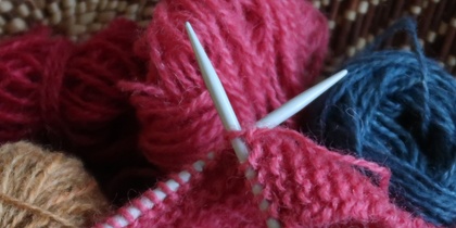 Närbild på stickning med rosa garn, stickor och garnnystan i olika färger.