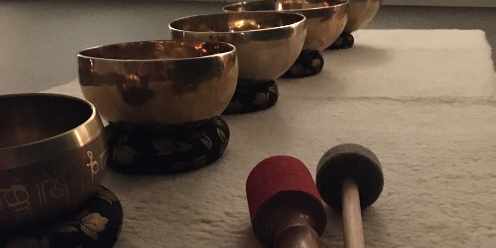 Fem tibetanska klangskålar står på rad på en matta med två klubbor framför dem i ett dämpat rum.