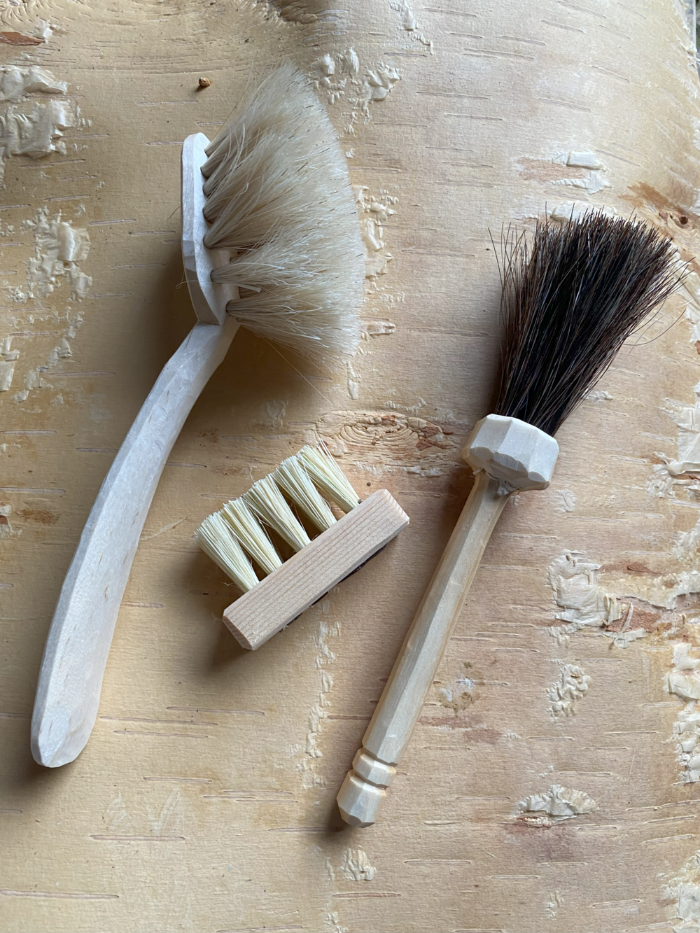 Tre olika borstar av trä och naturborst ligger på en ljus träyta.