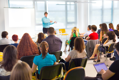 En grupp människor sitter i ett klassrum och lyssnar på en person som håller en presentation vid en whiteboard.