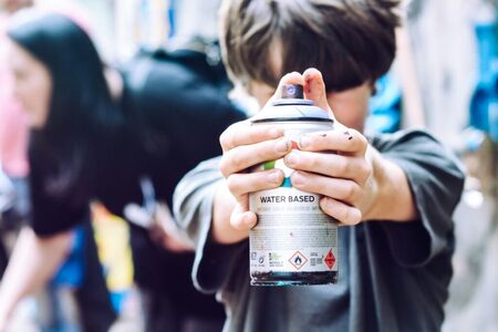 Barn håller en sprayburk med båda händer, fokus på burken, utomhusmiljö.