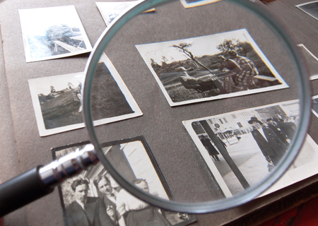 Ett fotoalbum med svartvita fotografier granskas med ett förstoringsglas.