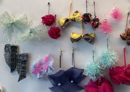 Färgglada dekorationer och accessoarer, som rosetter, blommor och tofsar, hänger på en vägg.