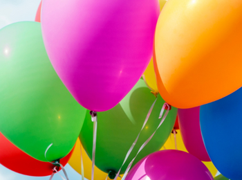 Flera färgglada ballonger svävar mot en blå himmel med vita moln.