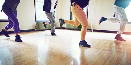 Fyra personer dansar i ett ljust rum med trägolv, endast deras ben och fötter syns.