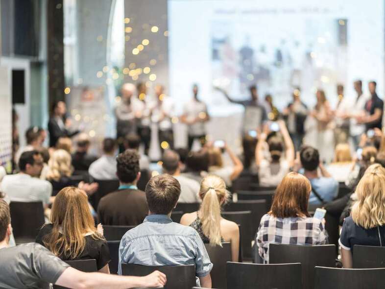 En aula full med folk som tittar på personer framme på scenen.