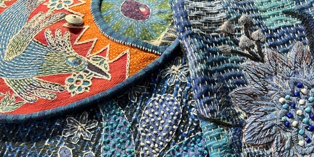 Detalj av färgglad broderad textil med blommor, fågel och pärlor i blå och röda nyanser.