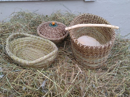 Tre handgjorda korgar av naturmaterial ligger på en hög med hö utomhus.