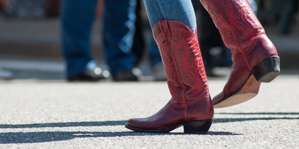 Person i blå jeans och röda cowboyboots dansar utomhus på asfalt.