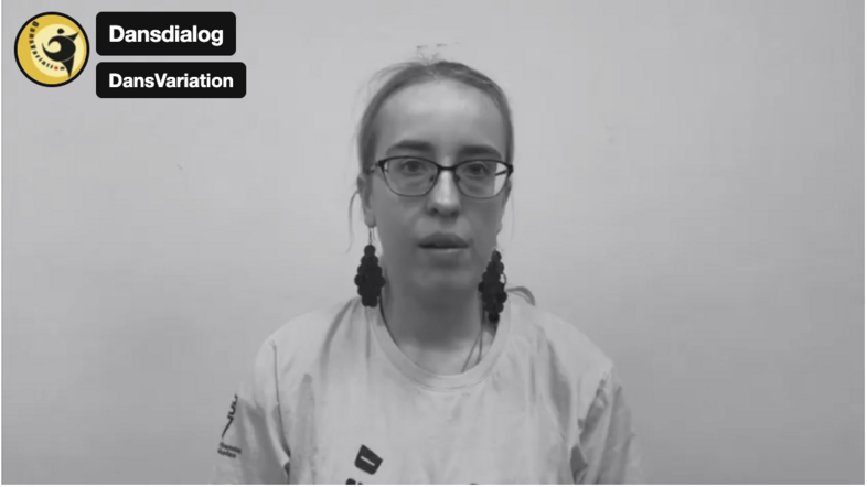 Person med ljust hår i fläta sitter mot en ljus bakgrund, bär en ljus t-shirt med tryck.