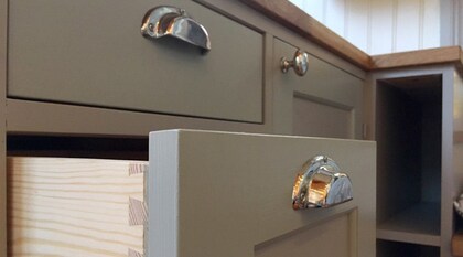 Närbild på gröna kökslådor och skåp med silverfärgade handtag, en låda är utdragen.