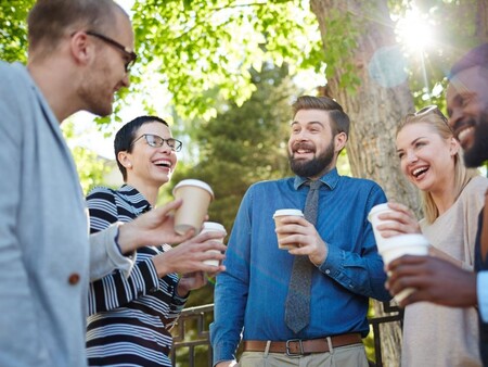 Fem personer står utomhus i fint väder och har kaffepaus.